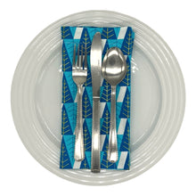 Load image into Gallery viewer, Cotton dinner napkin with contemporary blue and gold winter trees arranged as a places-setting with plate and cutlery.