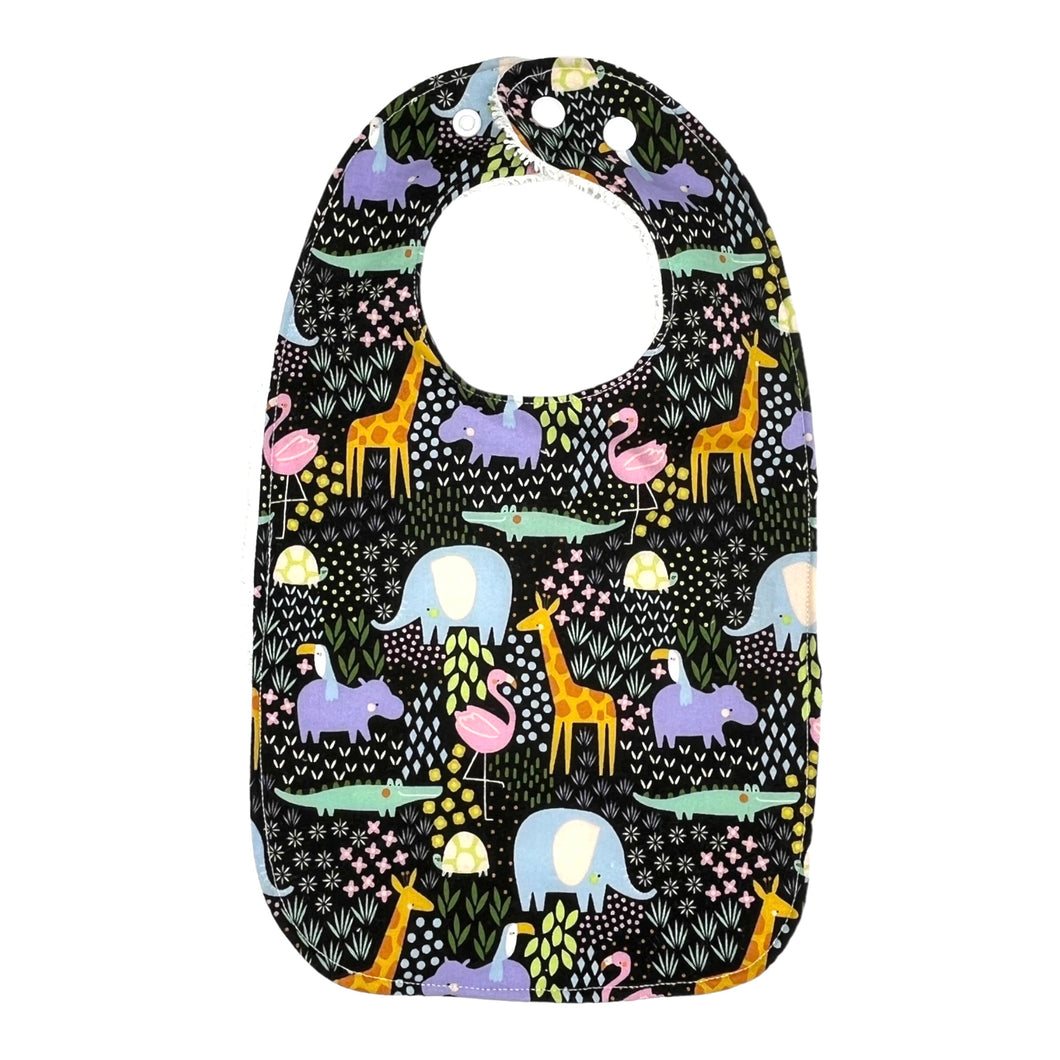 Baby bib Everyday Bib by Mimi's Little Loveys. Fun and vibrant design, featuring crocodiles, elephants, flamingos, giraffes, hippos, tortoises, plants, and flowers, on a black background. Backing is soft, white, terry cloth.