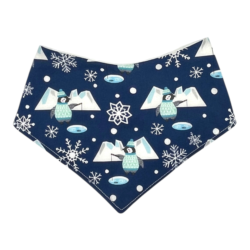 Baby bandana-style bib with penguins fishing, icebergs, and snowflakes, on a blue background.