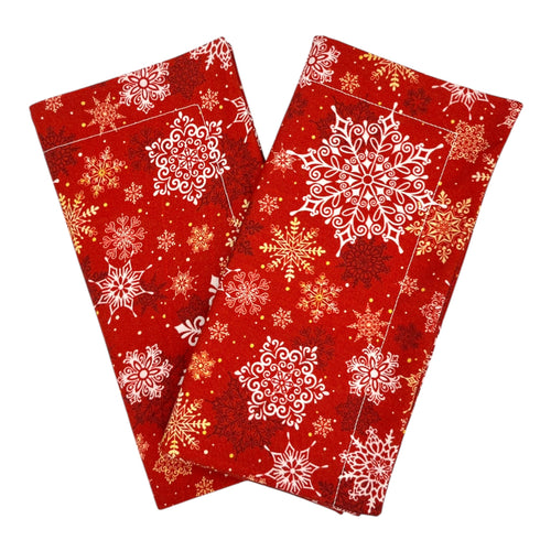 A set of two red dinner napkins with a white, gold, and red snowflake pattern.