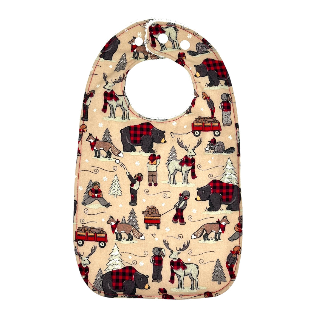 A baby bib with a fabric winter plaid pattern featuring bears, beavers, deer, and foxes in a snowy setting. 