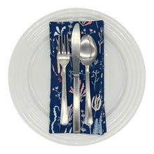 Load image into Gallery viewer, Folded navy blue napkin with coral and sea life design, on a white dinner plate with cutlery.
