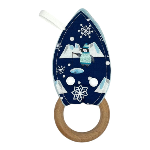 A teething toy featuring blue fabric with penguins fishing, icebergs, snowflakes, and a wooden ring.