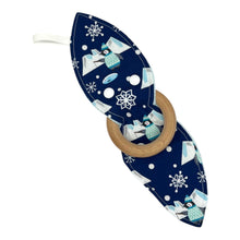Load image into Gallery viewer, A teething toy featuring blue fabric with penguins fishing, icebergs, snowflakes, and a wooden ring. Teether is unfastened to show both side of the design.
