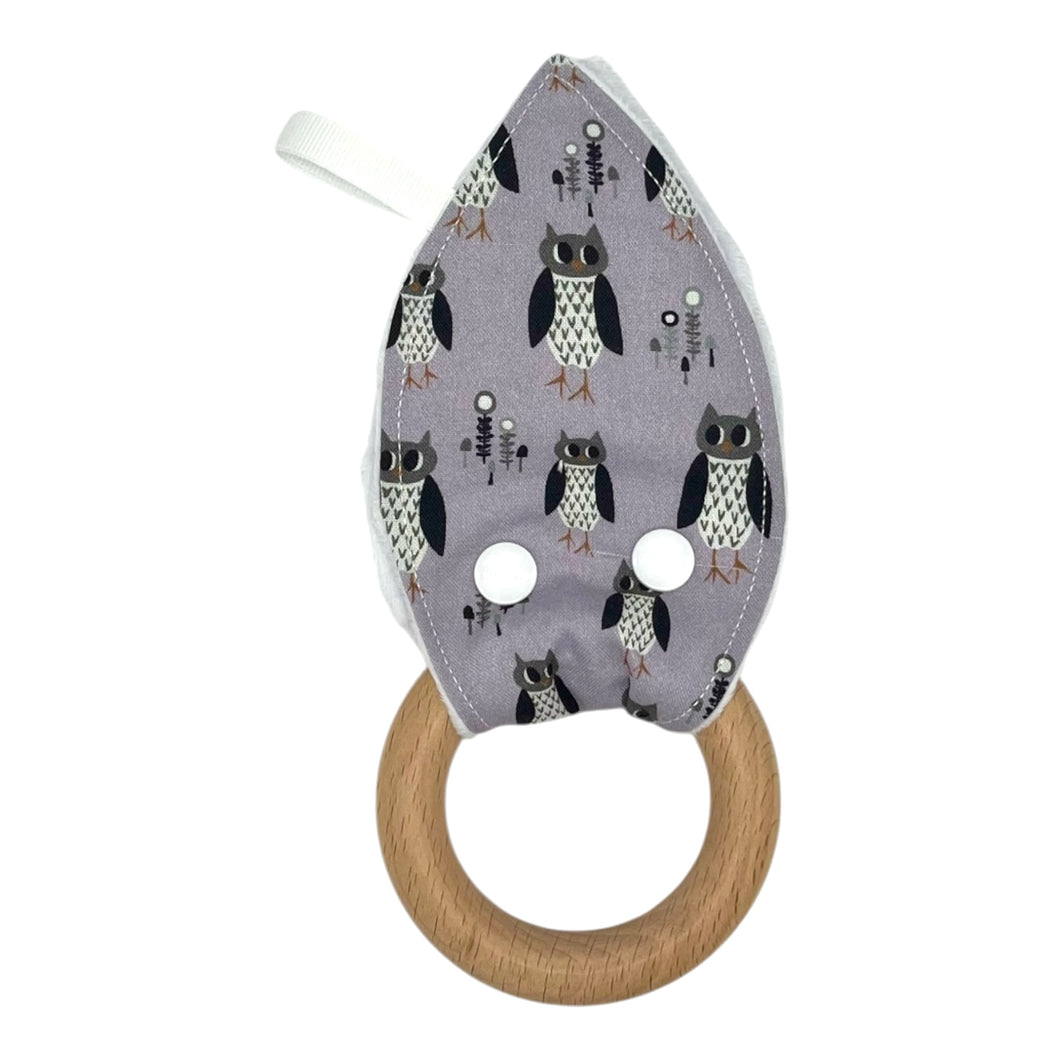 Teething ring with owl patterned fabric on a light purple background and wooden ring.